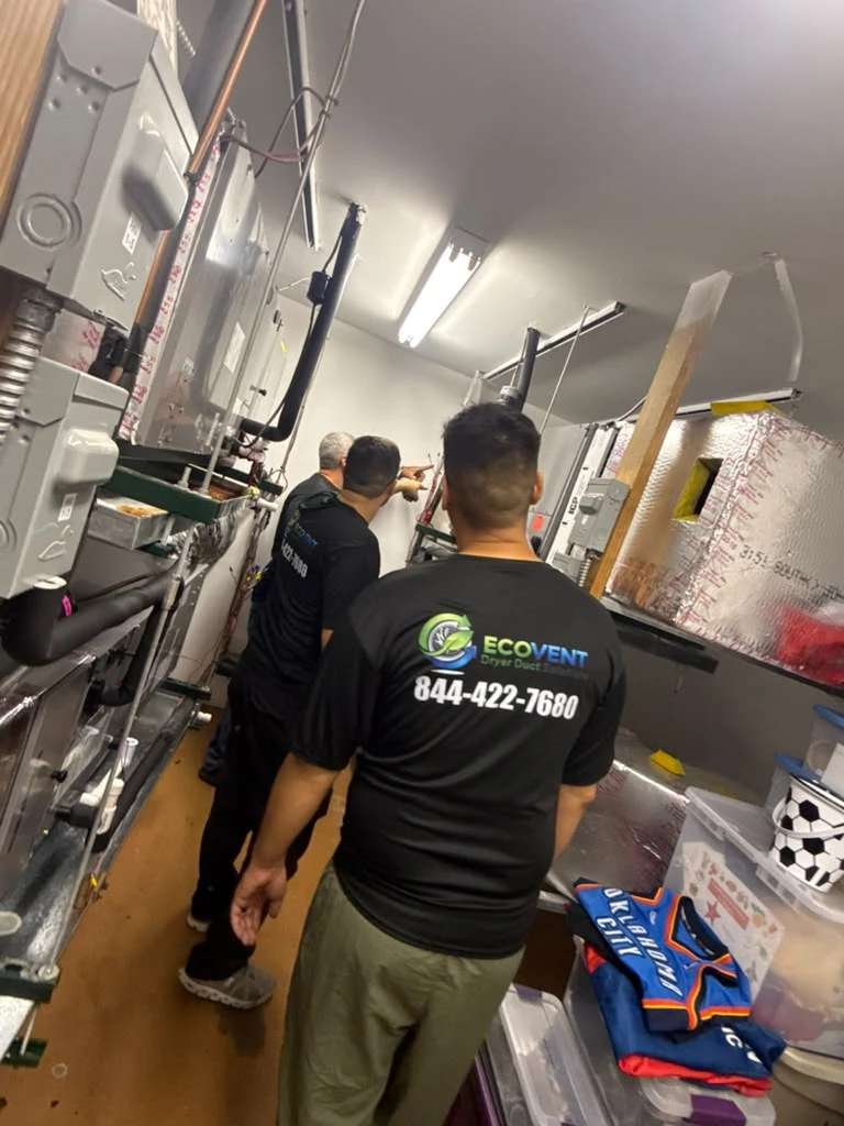 Three Ecovent technicians in company shirts looking over air-handler units in a commercial mechanical room