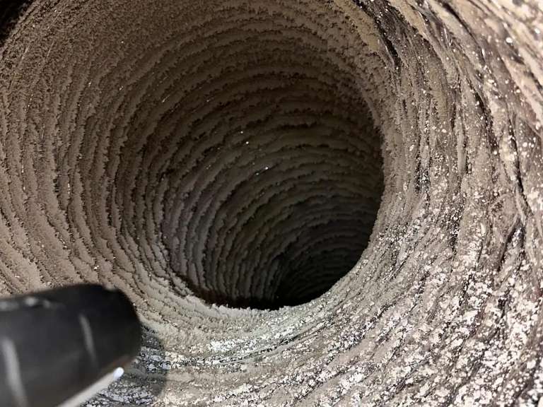 Inside a dryer exhaust duct caked with lint before cleaning, the brush just entering