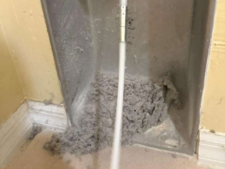 Lint piled at the base of a dryer vent wall box, the brush cable running into the run