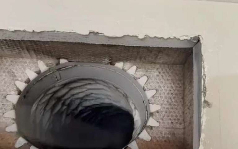 An air duct opened at a ceiling register, with the rotary brush cable inside the run