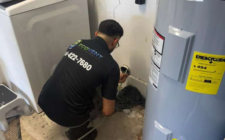 An Ecovent technician working the dryer vent connection between the washer and the water heater